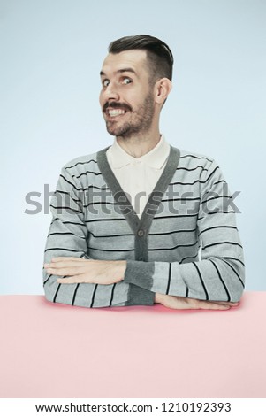 The happy and smiling business man sitting at table on blue studio background. The portrait in minimalism style