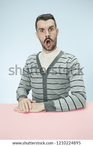 Surprised business man sitting at table on blue studio background. The portrait in minimalism style