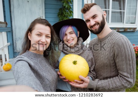 Three people in the background of the village house on the farm speak and laugh. A woman gives a pumpkin as a gift to the family. Working clothes, sweaters and a hat. Take selfie of themselves.