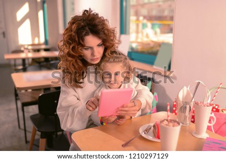 Have a look. Concentrated woman with curly hair staring at screen of her gadget while reading news