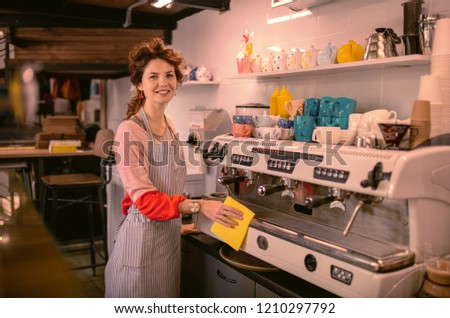Young barista. Charming young woman expressing positivity and cleaning equipment in cafe
