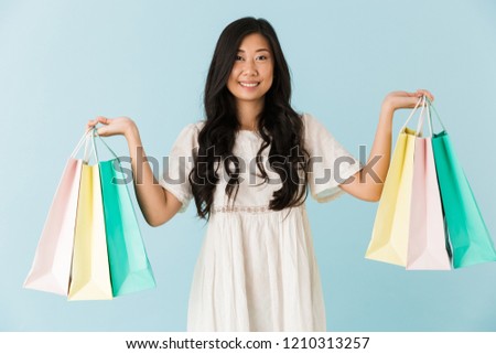 Image of asian young happy woman isolated over blue background holding shopping bags.