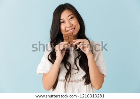 Image of young excited asian beautiful woman isolated over blue background eat chocolate.