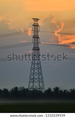 Silhouette high voltage In the middle of the field alone in the early morning of the rainy season and rain clouds are forming behind.