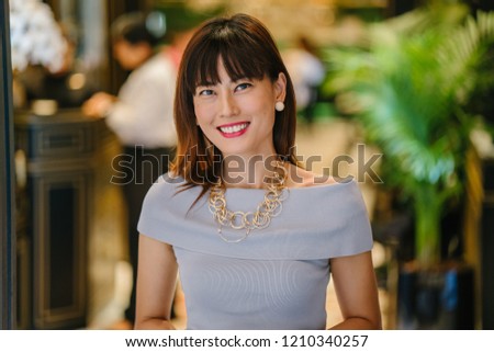 A close up portrait of a smiling and laughing Asian Chinese woman. She is middle-aged, elegant, attractive and laughing candidly for her head shot. 