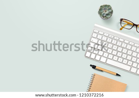 neat and clean, well organized home office workspace with technical gadgets, writing supplies, computer keyboard, glasses and a potted succulent plant on a mint background