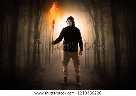 Mysterious man coming from a path in the forest with burning flambeau concept