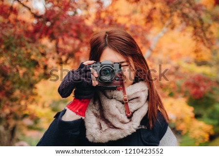 Pretty asian woman on wear winter cloth holding camera and shooting on beautiful autumn leave trees background in japan.
