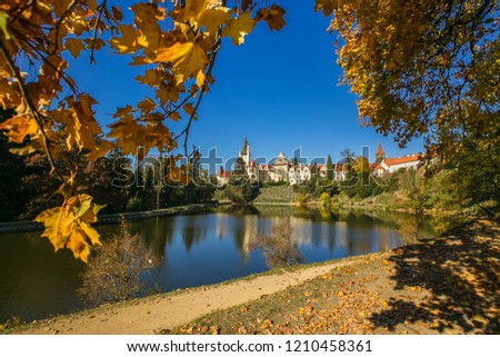 Beautiful fall scenery of famous Pruhonice castle, Czech Republic, Europe, standing on hill, sunny day, blue sky, reflection in lake, yellow maple leaves framing picture, shadow of colorful trees