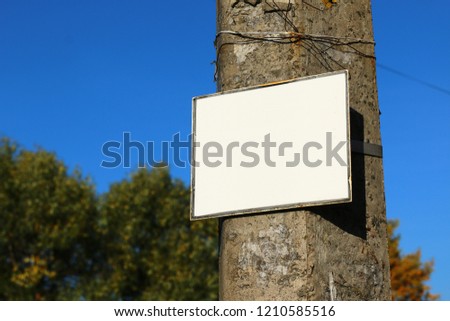Old blank sign on a pole against the background of the forest and the sky