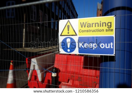 Warning sign construction site, keep out. Bright signs put on metal mesh fence on work area. Space to add text on orange, white plastic barriers & blur building in background. Health & Safety concept 