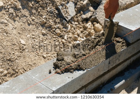 Masonry worker make concrete wall by cement brick and plaster at construction site, a spatula in the hands