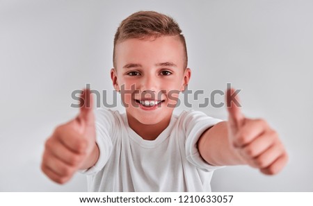 Portrait of a cute boy on a gray background, who makes a gesture with a thumbs up. Head shot of handsome funny boy, isolated on gray background. Happy child looking at camera.