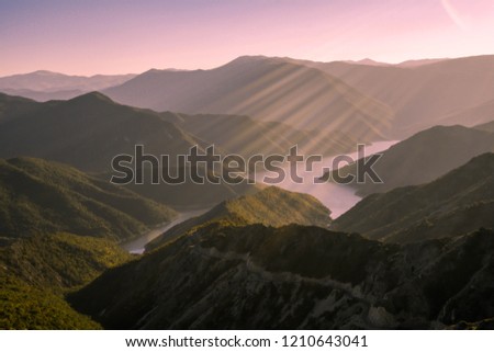 Landscape shot of a lake surrounded by mountains, sun rays falling down in the centre of the photo, pink hue