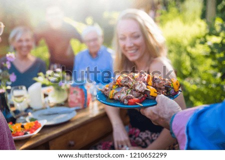 In the summer, a family of three generations gathered around a table in the garden to share a barbecue. close-up on a grilled meat dish presented to the guests