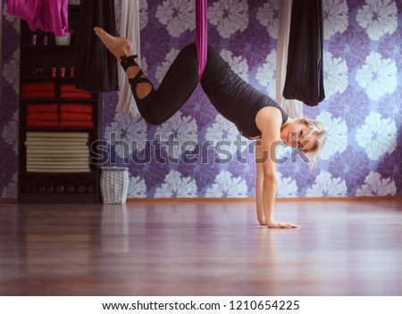 Young woman doing aerial yoga practice in purple hammock in fitness club.