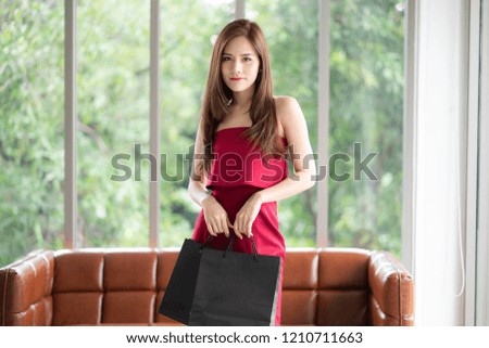 A beautiful girl in red dress is holding many shopping bags. She is buying more things for herself.