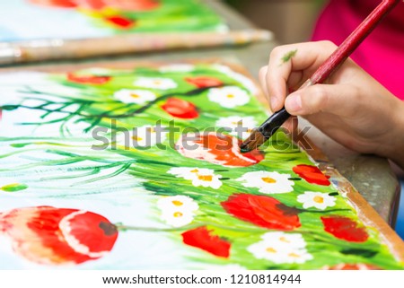 Child paints a picture by gouache. Kid drawing poppies and chamomiles. The hand and paint brush. Closeup, selective focus