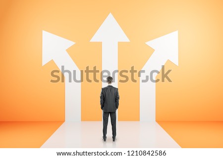 Back view of young businessman standing on orange background with three arrows. Different direction and success concept