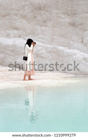 A young woman photographs the mountains of Pamukkale in Turkey and her figure is reflected in the water
