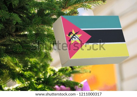 Mozambique flag printed on a Christmas gift box. Printed present box decorations on a Xmas tree branch. Christmas shopping in Mozambique, sale and deals concept.