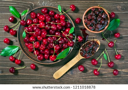 Red cherries, green leaves and cherry jam on a dark wooden table. Rustic style, top view.