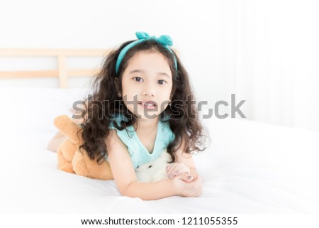 attractive asian children rest on white bed, she feeling happy, curly hair
