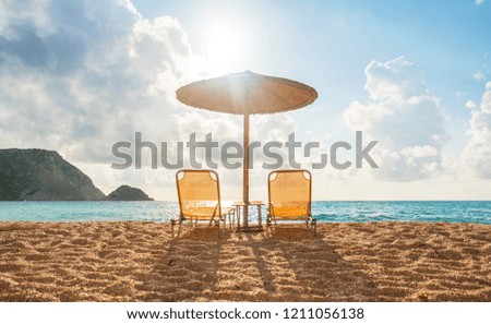Two sun beds and an umbrella on sea side awaiting for tourists for sunset watching. Perfect vacation picture.