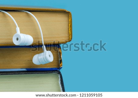 A white headphones and books on a blue background. Audio book concept. Copy space 