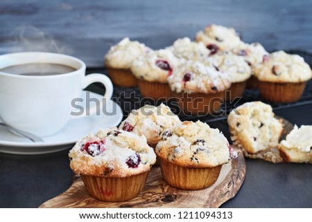 Cranberry Muffins on a wood cutting board with more cooling on a bakers rack. Extreme shallow depth of field with selective focus on center muffin. Steaming hot cup of coffee in the background.