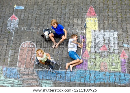 Two little kids boys and cute toddler girl drawing knight castle with colorful chalks on asphalt. Happy siblings and friends having fun with creating chalk picture and painting