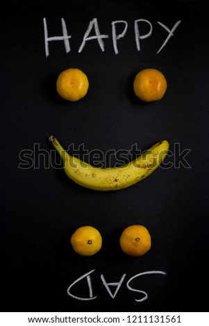 Happy or sad ? Creative layout made with banana and mandarins on black background in shape of happy or sad face emotion. States of mind and daily change of mood concept. Invertible photo. Flat lay