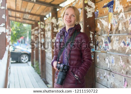 Woman photographer with a camera on a wooden background in a warm jacket in the autumn.