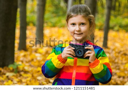 A little girl takes pictures on the background of yellow leaves in the autumn Park.