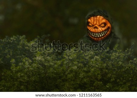 Creepy angry pumpkin head with sharp teeth walks about the shadows of the night. Scary mean pumpkin head looks over behind the bush. 