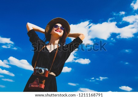 photo of the beautiful young woman with camera on the sky background