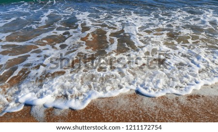 Sea water with white foam in the coastal sand, natural close-up background