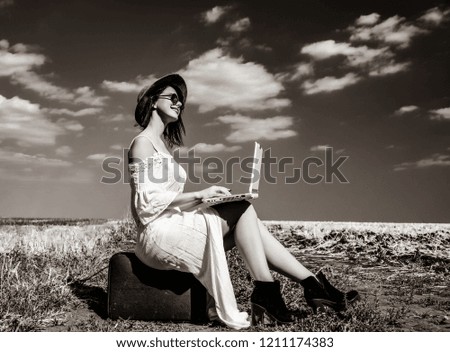photo of the beautiful young woman sitting on the suitcase with laptop in the field