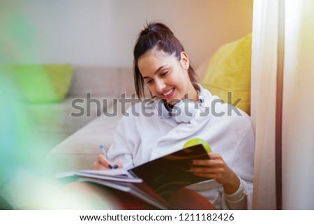 Cute young girl listening to the music and looking at the tablet. Headset around her neck and sitting in bathrobe.