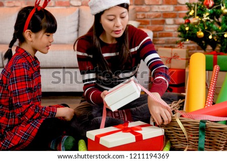 Happy mother and daughter sitting on floor at xmas tree and packing gift box for Christmas present. young mom and childhood in the living room doing teamwork preparing for the holidays concept.