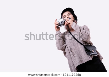 Portrait of young attractive woman in black cap, torn sweater, with blue lips, pink hair, takes a photo by retro camera, isolated on white background with copy-space