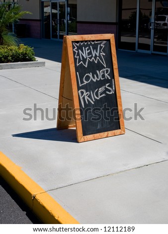 Blackboard sign that says lower prices on sidewalk