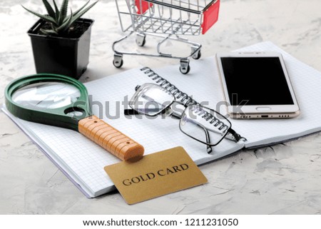 The concept of online shopping. Composition with discount cards and shopping trolley and telephone on a light background.