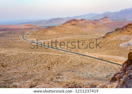 Endless old road trough the western desert in California. Arid and dry texture. Colorful mountains.