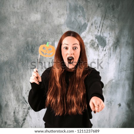 Surprised young woman holding a Halloween pumpkin sign while pointing her finger against a grunge background