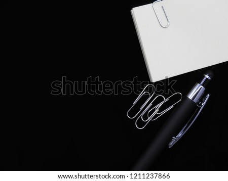 White paper with pen and paper clips on black blackground. 
