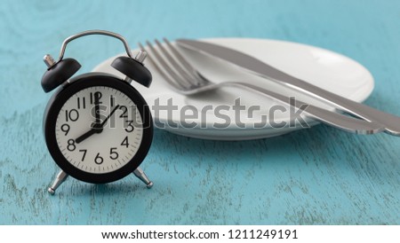 Intermittent fasting concept with clock, white plate, fork and knife on blue table Royalty-Free Stock Photo #1211249191