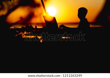 silhouette of a young man painting a picture with paints on canvas on an easel outdoors, boy with paint brush and palette engaged in art on nature in a field at sunset