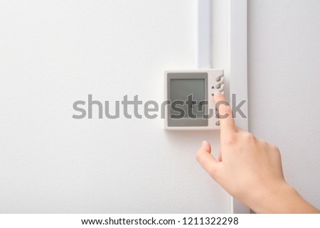 Woman adjusting thermostat on white wall, closeup. Heating system Royalty-Free Stock Photo #1211322298