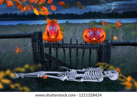 Two funny carved halloween pumpkins on a wooden fence with skeleton in foreground and thunderstorm in the background